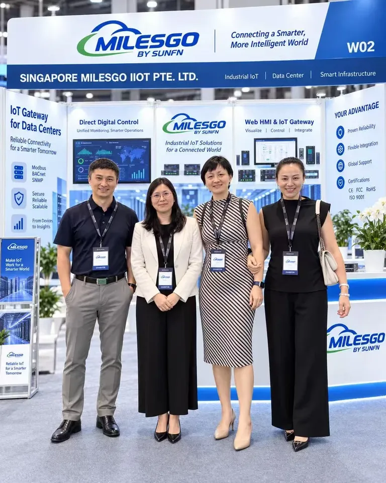 أربعة أشخاص في جناح Singapore Milesgo IIoT Pte. Ltd. رقم W02، أمام لوحات بوابات إنترنت الأشياء لمراكز البيانات والتحكم الرقمي المباشر وWeb HMI وبوابة إنترنت الأشياء.